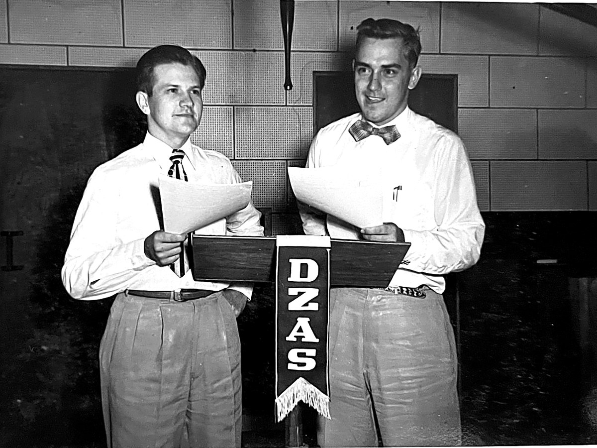Ken Engle and Ken Brooks at the microphone stand marked DZAS, holding scripts, live on the air in Manila