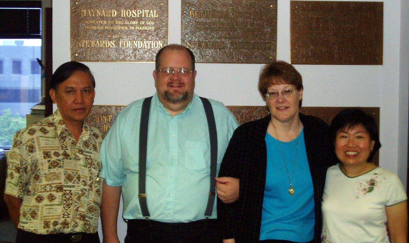 Kevin and Cheryl (center) with guests from Singapore in the Foundation office, in front of the bronze plaques from the Foundation's hospitals, among them Maynard Hospital and Bethesda Hospital. Stewards Foundation once owned six hospitals.