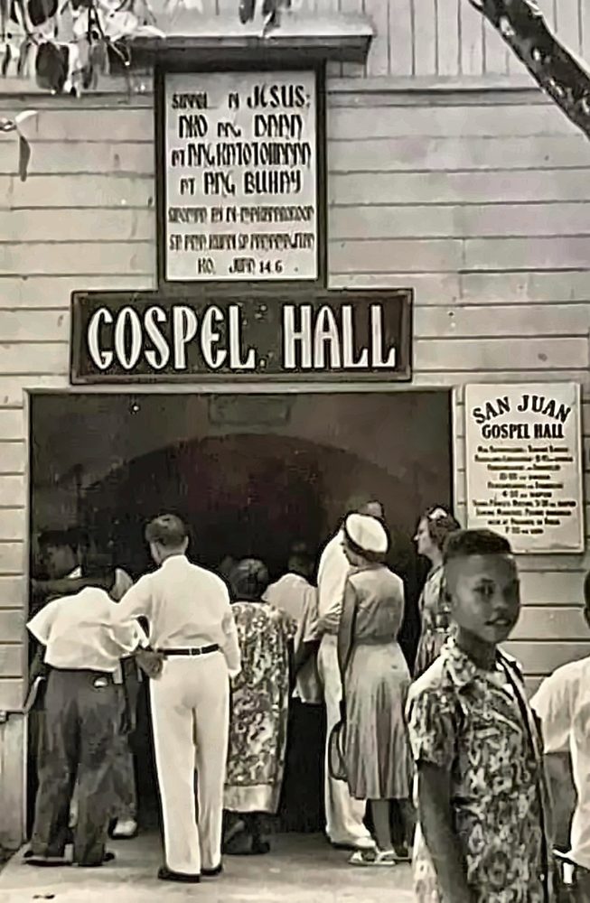 Ang San Juan Gospel Hall sa Maynila: mga taong pumapasok sa ilalim ng karatulang GOSPEL HALL, at isang batang nakasuot ng de-disenyong polo sa harapan